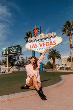 a woman posing in front of the welcome to las vegas sign with her legs crossed