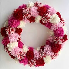 a pink, red and white wreath with pom - poms