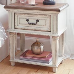 a table with a vase on top of it next to a lamp and books in front of a bed