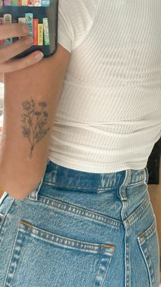 a woman with a flower tattoo on her arm holding a cell phone in her hand