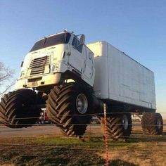 a large white truck with huge tires on it's front wheels parked in a field