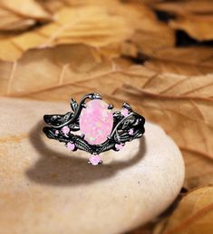 a pink opalite ring sitting on top of a leaf covered ground with leaves around it