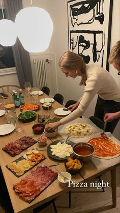 two people preparing food at a table with plates and bowls on it, while another person stands in front of the table