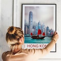 a woman holding up a poster with a boat in hong kong on it's side