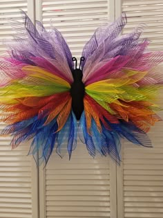 a multicolored butterfly decoration hanging on the wall with shutters in the background