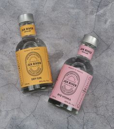 three bottles of gin are sitting on the ground, one pink and one yellow with silver caps