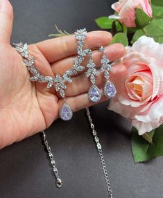 a person holding two pieces of jewelry in their hand next to a pink flower and rose