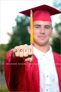 a young man wearing a graduation cap and gown pointing at the camera with his fist