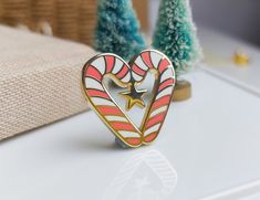 a heart shaped pin sitting on top of a white table next to small christmas trees