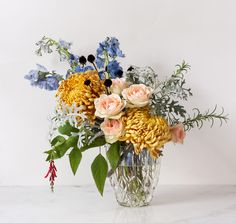 a vase filled with lots of flowers on top of a white counter next to a wall