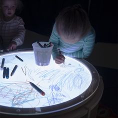 two children are sitting at a table with some writing on it and one child is drawing