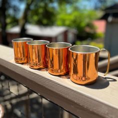 three copper mugs are lined up on a ledge