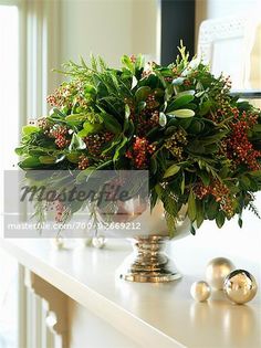 a white table topped with a metal vase filled with flowers and greenery next to christmas decorations