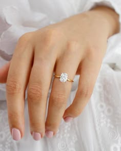 a woman's hand with a diamond ring on her left hand, wearing a white dress