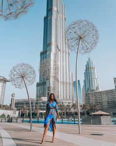 a woman standing in front of a tall building with dandelions hanging from it