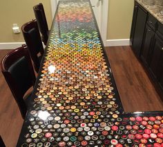 a long table covered in lots of different colored bottle caps on top of a wooden floor