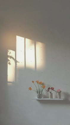 three white vases with flowers in them on a shelf next to a window,