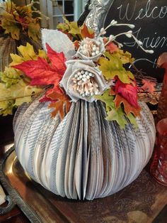 an origami pumpkin decorated with leaves and flowers on top of a wooden tray