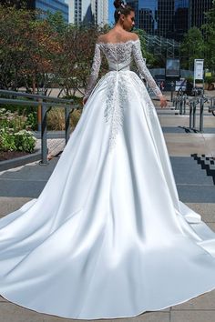 a woman in a white wedding dress is standing on the sidewalk with her back to the camera