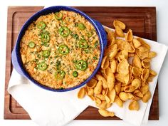 a blue bowl filled with cheese and green peppers next to chips on a wooden tray