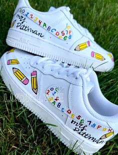 a pair of white shoes with school supplies painted on them sitting in the green grass