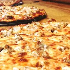 two pizzas sitting on top of a table covered in cheese and meat toppings