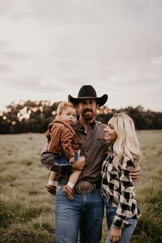 a man and woman are standing in a field with their baby son, who is wearing a cowboy hat