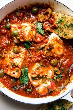 a pan filled with meat and vegetables covered in tomato sauce next to some pita bread