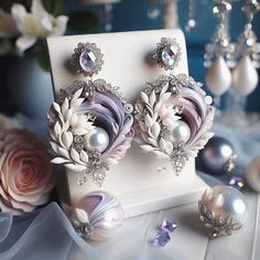 a pair of white and purple earrings sitting on top of a table next to flowers