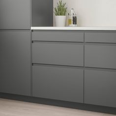 a kitchen with gray cabinets and white counter tops, along with a potted plant