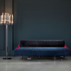 a blue velvet couch sitting in front of a tall light pole with candles on it