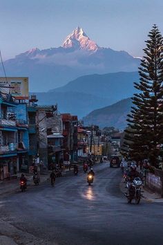 motorcycles are driving down the street in front of some buildings with mountains in the background