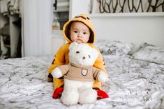 a little boy sitting on top of a bed holding a teddy bear