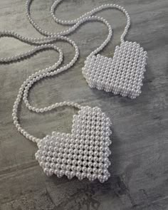 two white beaded purses on a gray surface with one being held by a chain