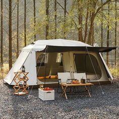 a tent is set up in the woods with two chairs and a table on it