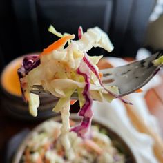 a fork full of coleslaw is being lifted from a bowl