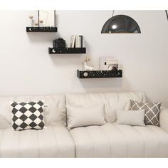 a living room with white couches, black and white pillows and shelves on the wall