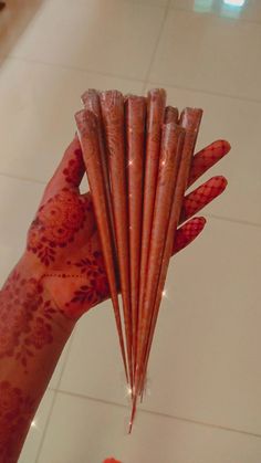 a person holding up several sticks with red paint all over their body and hands, in front of a white tiled wall