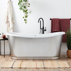 a white bath tub sitting on top of a wooden floor next to a potted plant