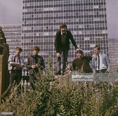 a group of young men standing next to each other in front of tall buildings on a cloudy day