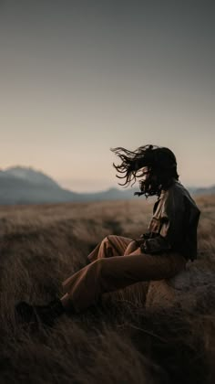 a man sitting on top of a rock in the middle of a dry grass field