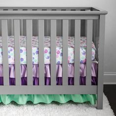 a gray crib with purple and green bedding