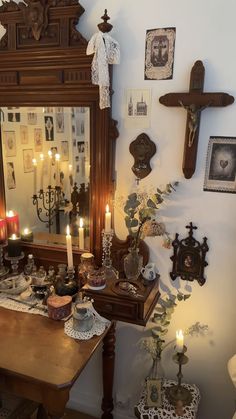 a wooden table topped with lots of candles next to a wall filled with pictures and crosses