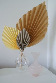 a vase with a paper fan on top of it next to a small glass vase