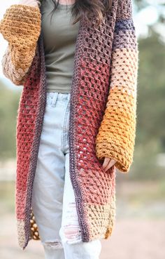 a woman is wearing a colorful cardigan sweater and white jeans with her hands in her pockets