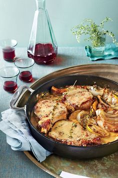 a pan filled with meat and vegetables on top of a table next to glasses of wine