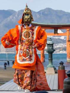 a person dressed in an orange and white costume walking on a pier near the water