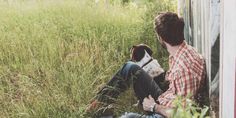 a man sitting in the grass with his dog next to him and looking at something