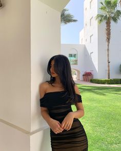 a woman leaning against the side of a building wearing a black dress with sheer panels