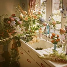 a kitchen sink filled with lots of flowers and greenery next to a window covered in curtains